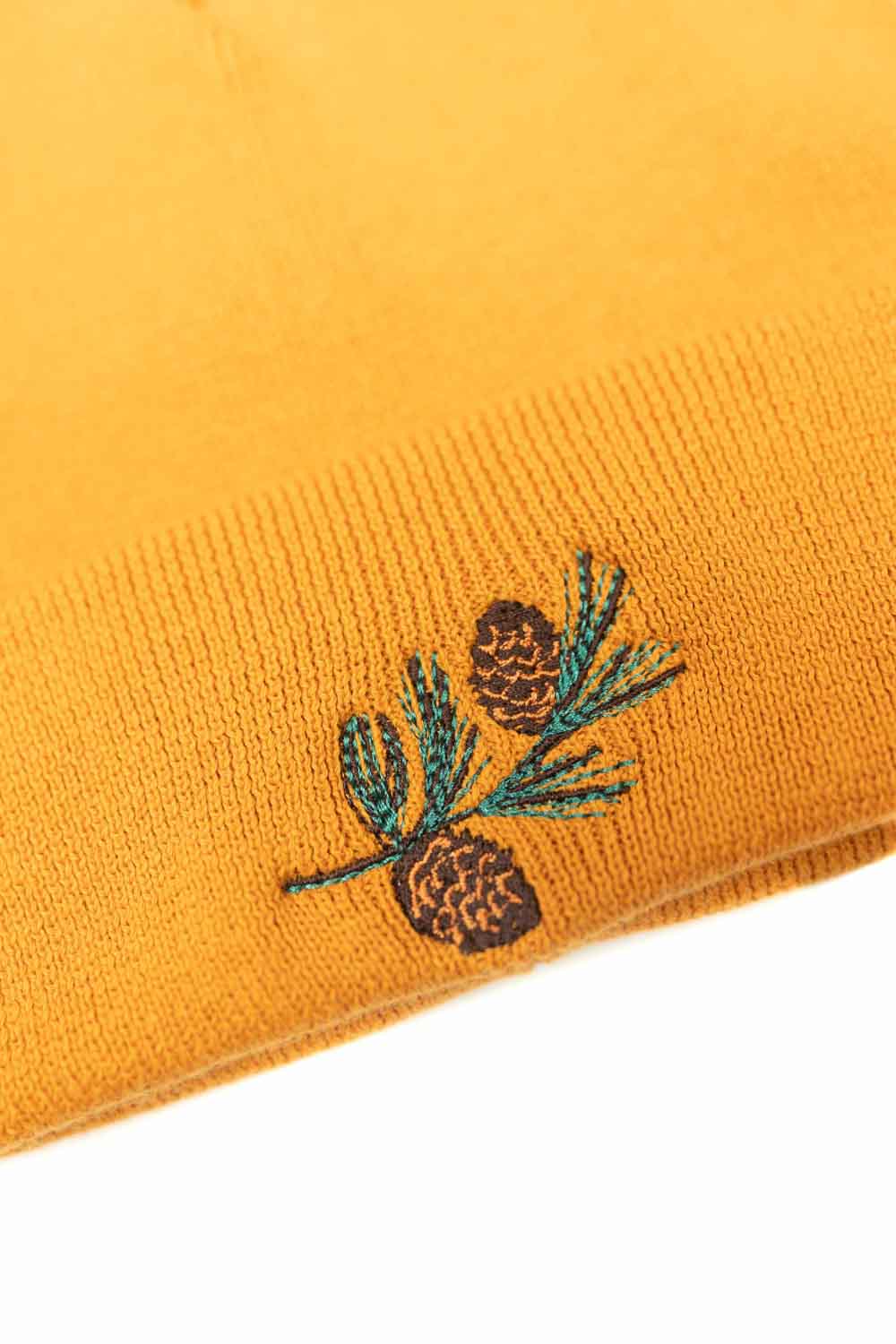 Căciulă portocalie din tricot reiat cu manșetă întoarsă, brodată cu o ramură de pin și conuri de brad, un accesoriu inspirat de natură pentru un stil casual și elegant.