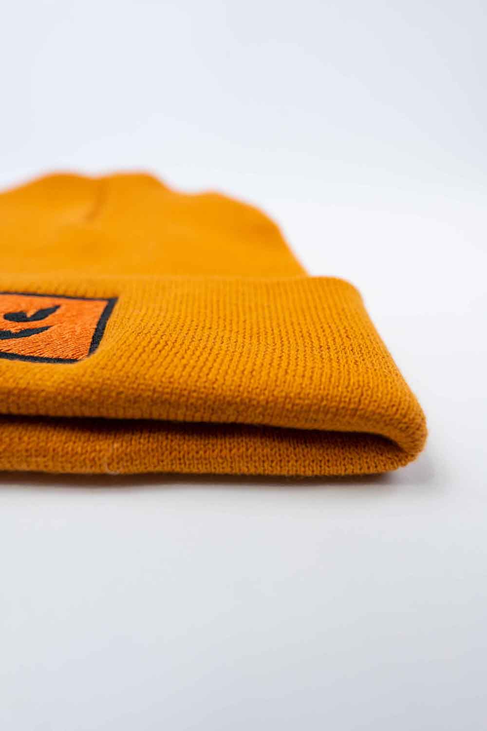 Căciulă portocalie din tricot reiat cu manșetă întoarsă, brodată cu o față de dovleac Jack-o'-lantern neagră într-un chenar dreptunghiular, un accesoriu amuzant inspirat de Halloween.