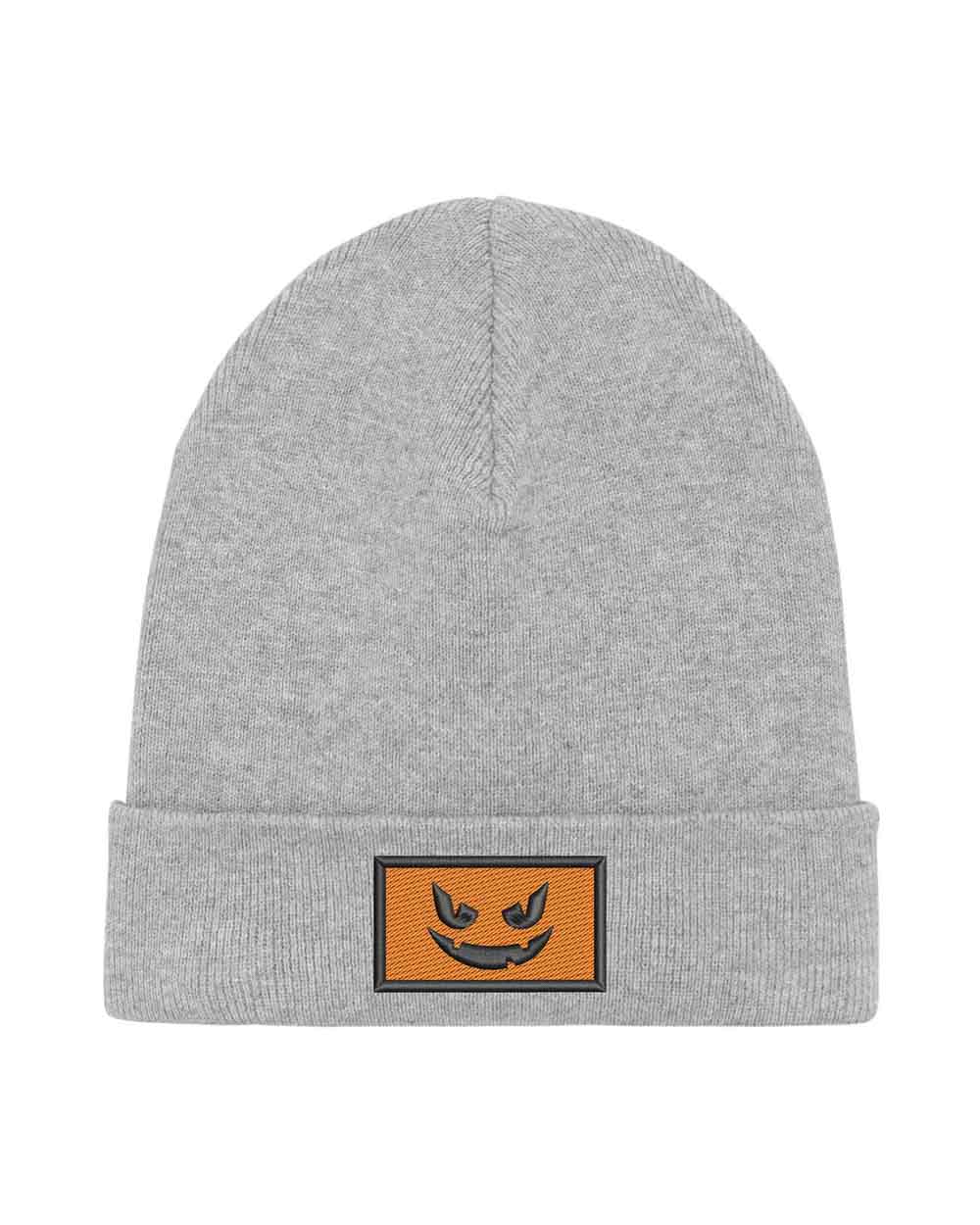 Căciulă gri din tricot reiat cu manșetă întoarsă, brodată cu o față de dovleac Jack-o'-lantern neagră într-un chenar dreptunghiular, un accesoriu amuzant inspirat de Halloween.