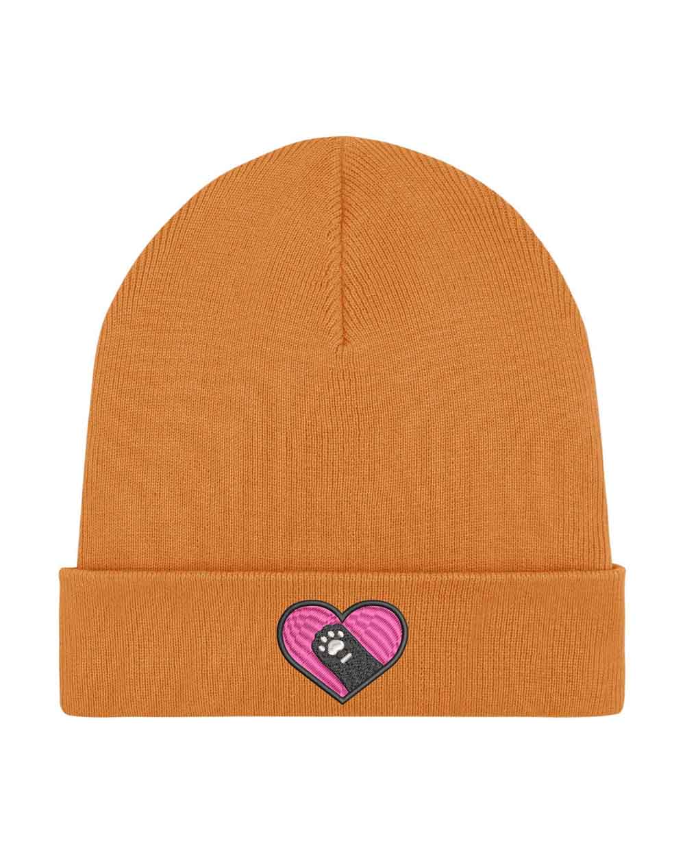 Căciulă portocalie din tricot cu manșetă întoarsă, brodată cu un patch roz în formă de inimă și o lăbuță neagră în centru, un accesoriu adorabil pentru iubitorii de animale.