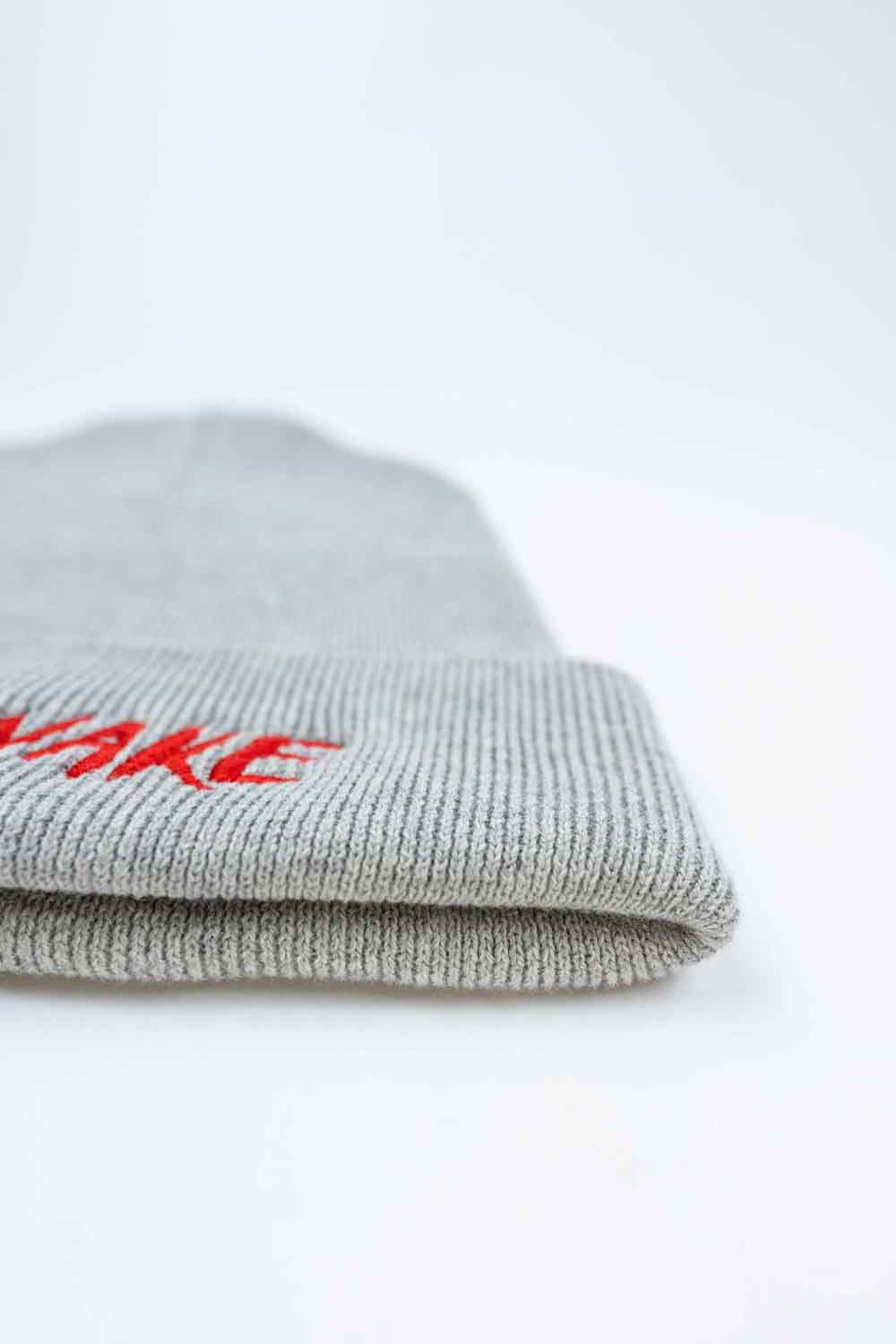 Căciulă gri din tricot cu manșetă întoarsă, brodată cu mesajul „Stay Awake” în roșu și un mic design de pânză de păianjen neagră, un accesoriu original și amuzant pentru un stil casual.