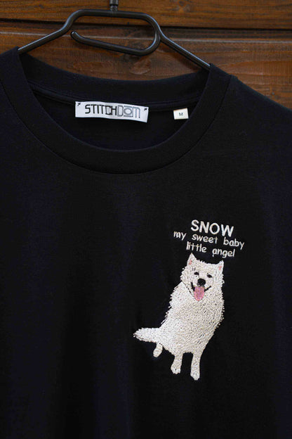 Tricou negru cu model brodat reprezentând un câine și text, pe o suprafață din lemn.