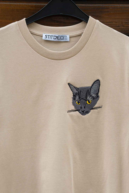 Tricou bej cu model brodat reprezentând fața unei pisici, pe umeraș.