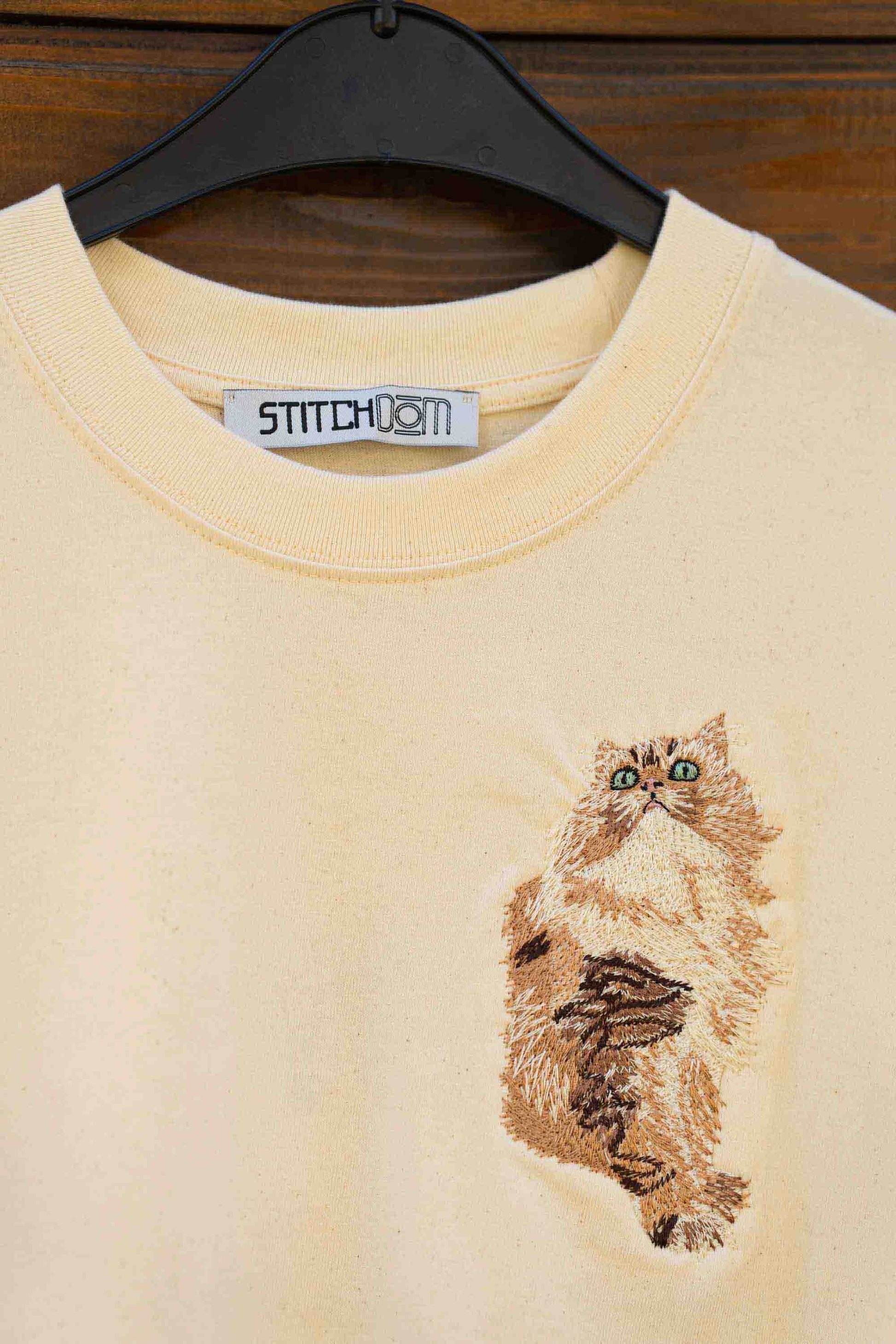 Tricou bej cu model brodat reprezentând o pisică.