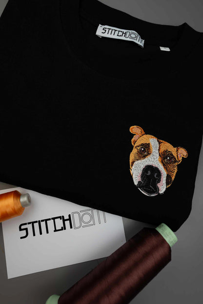 Tricou negru cu guler rotund, cu un model brodat detaliat reprezentând fața unui câine pe partea stângă a pieptului, așezat plat pe un fundal gri închis, cu conuri de ață și un card branduit Stitchdom vizibile.