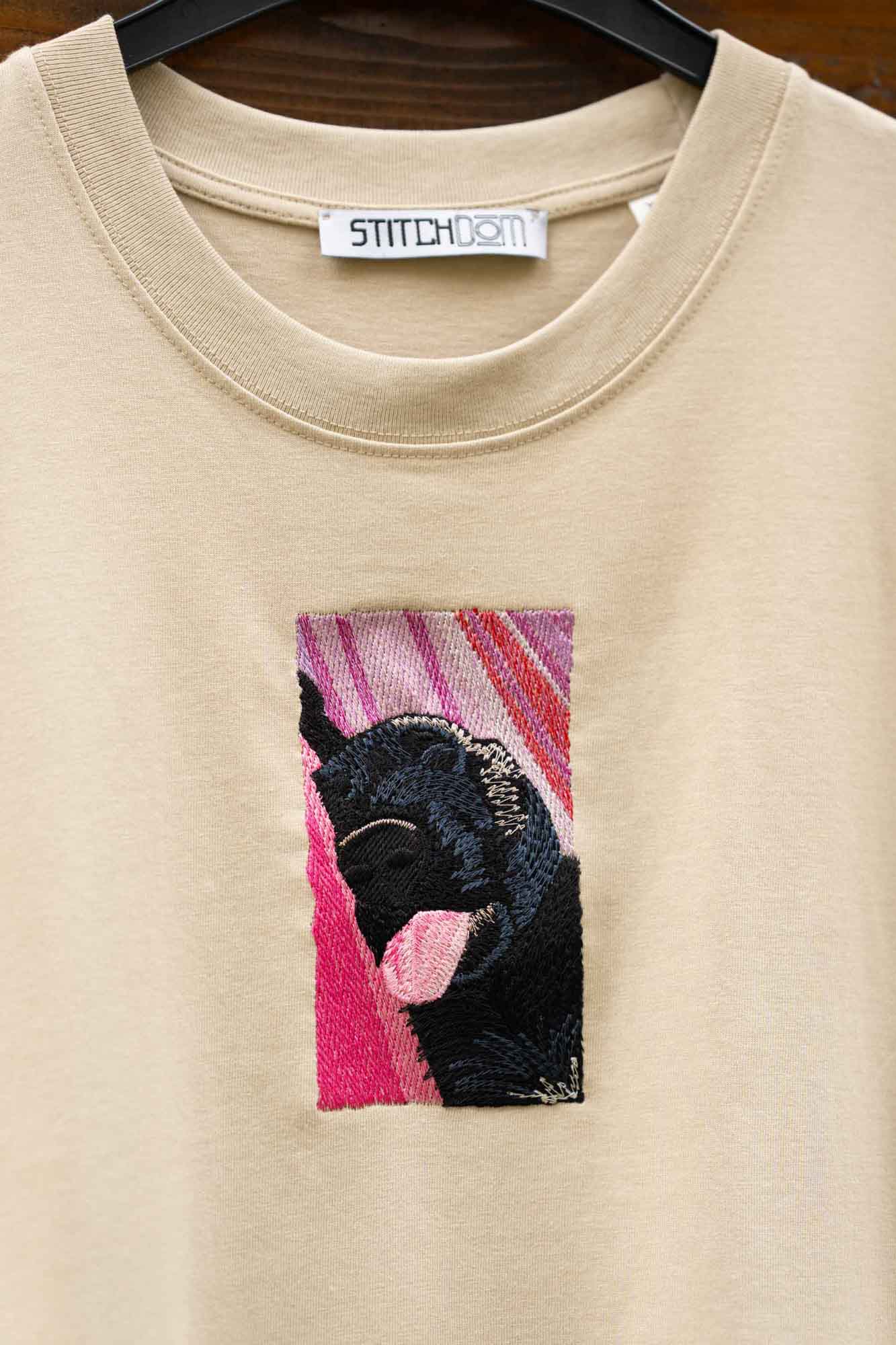 Tricou bej cu model brodat cu un câine negru care doarme, pe sezlong.