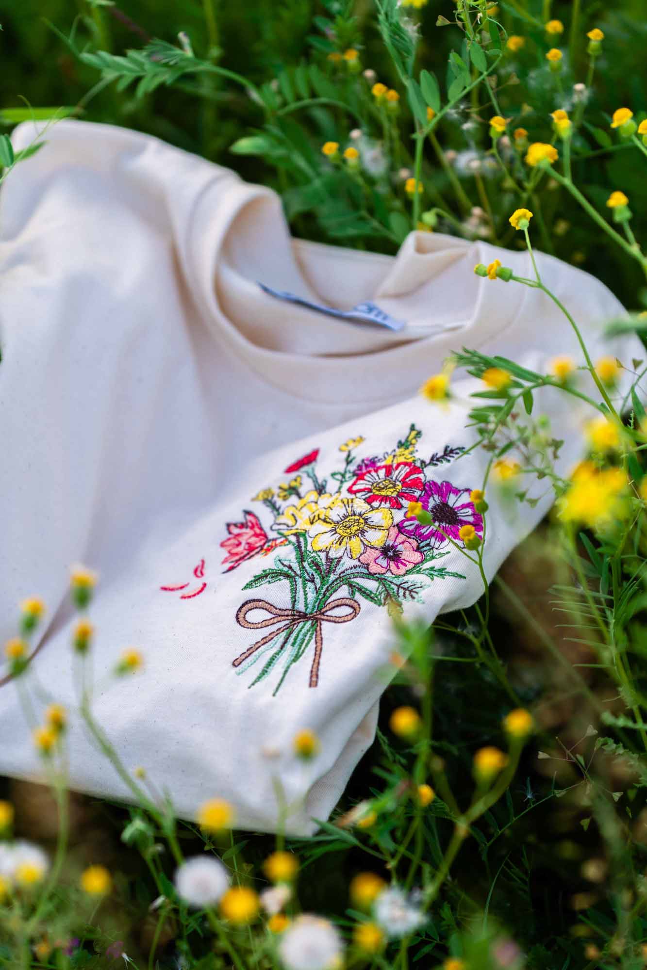 Tricou alb din bumbac organic, cu o poză brodată florală într-un câmp cu flori sălbatice.