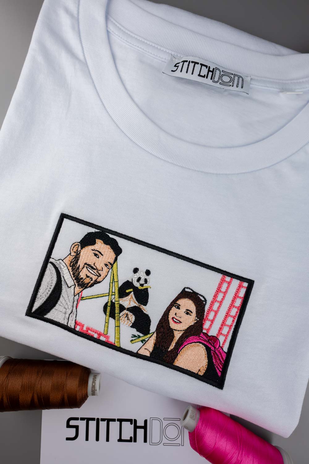 Tricou alb din bumbac organic, împăturit, cu un portret brodat personalizat în formă de patch dreptunghiular pe piept, pe un fundal gri, alături de conuri de ață.