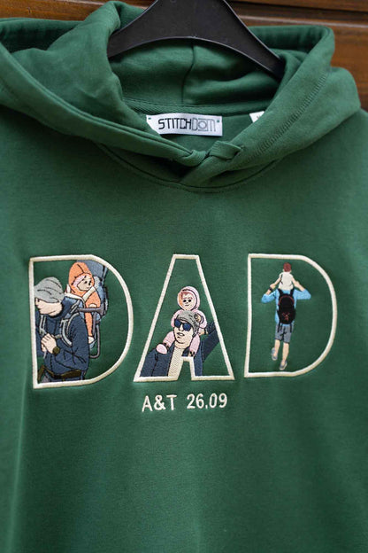 Hanorac verde cu glugă, pe umeraș, cu designul „DAD” brodat, fiecare literă conținând elemente brodate.