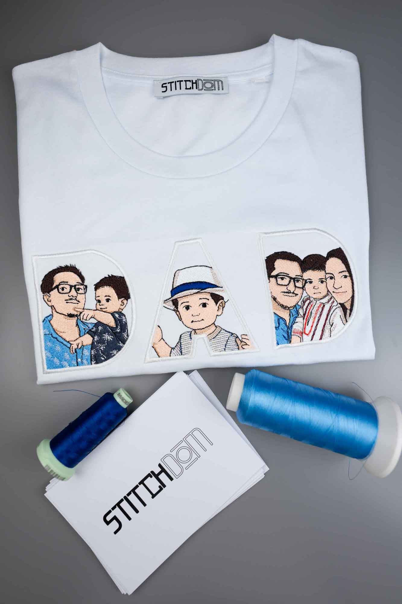 Tricou alb împăturit cu textul „DAD” brodat, fiecare literă conținând câte o imagine brodată, pe un fundal gri, alături de conuri de ață.