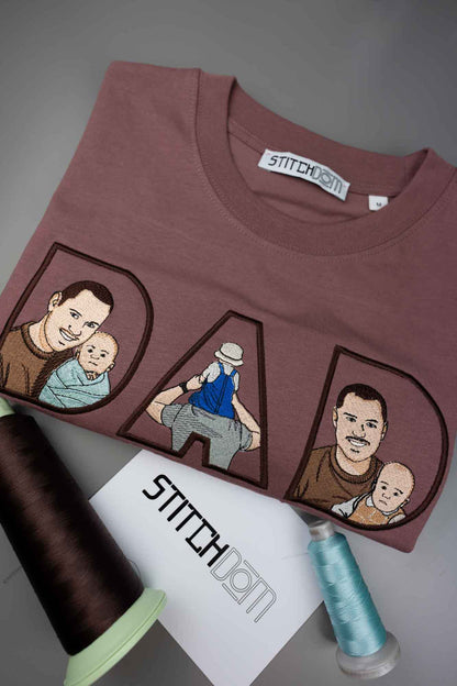 Tricou maro cu textul „DAD” brodat în litere mari, fiecare literă conținând o ilustrație brodată reprezentând un tată și un copil, pe fundal gri, alături de conuri de ață.