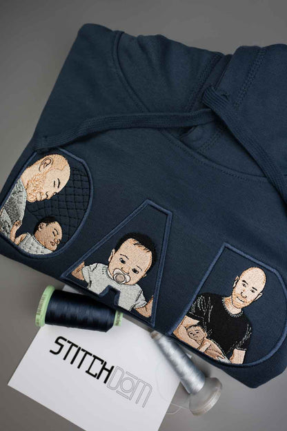 Tricou bleumarin din bumbac organic, împăturit, cu poze brodate personalizate cu trei bebeluși, alături de un con de ață neagră și un card „Stitchdom”, pe un fundal gri.