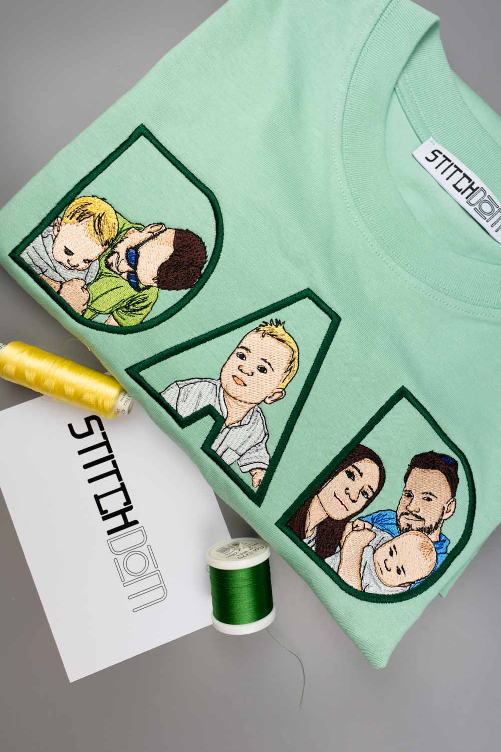 Tricou verde mentă din bumbac organic, cu textul „DAD” realizat din litere mari brodate, fiecare literă având în interior o poză de familie brodată personalizat, pe un fundal gri, alături de conuri de ață verde și galbenă și un card alb cu brandul „STITCHDOM”.