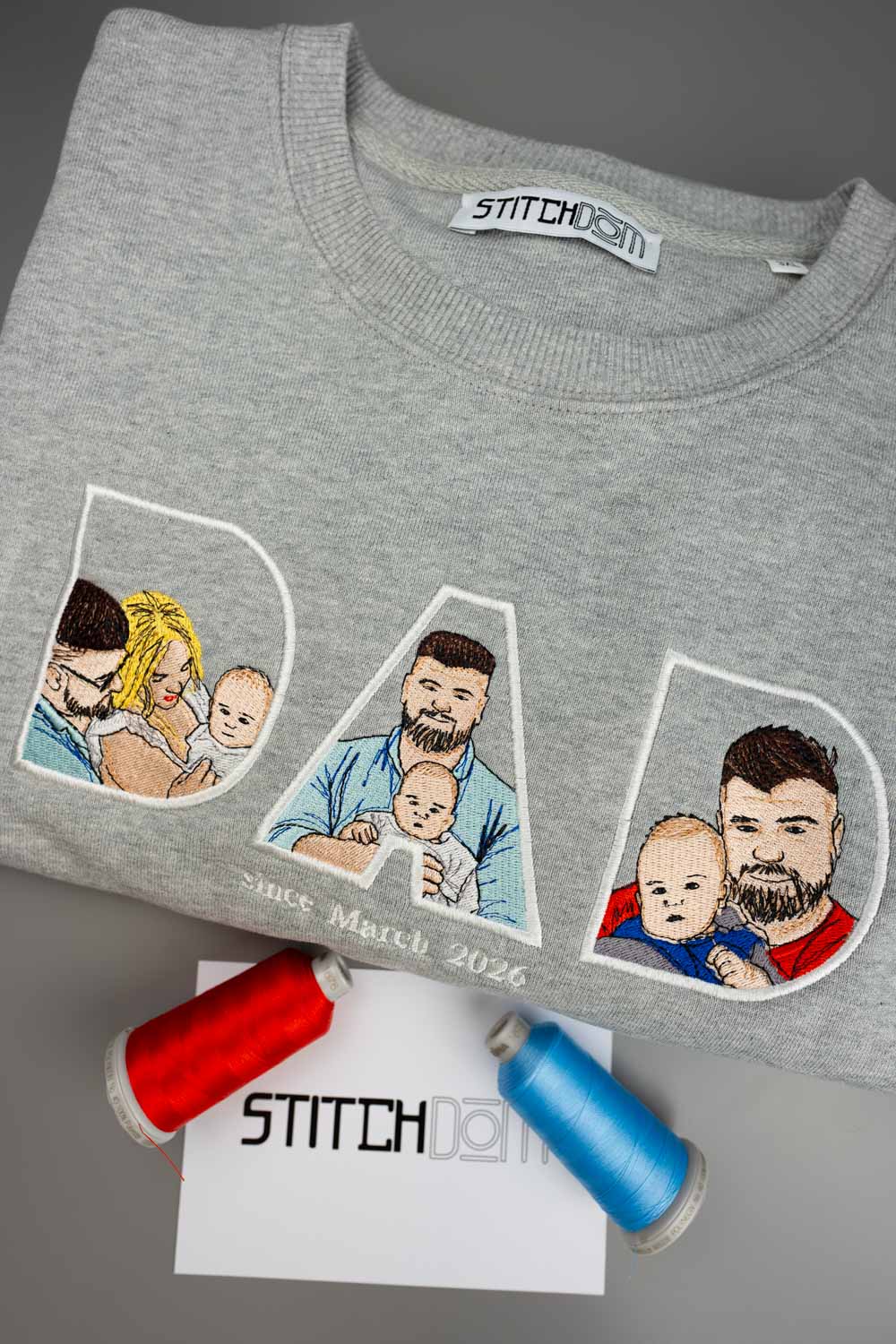 Bluza gri deschis melanj din bumbac organic, împăturit, cu textul „DAD” brodat și portrete brodate cu un tată și copiii săi, iar dedesubt textul „Since March 2026”.