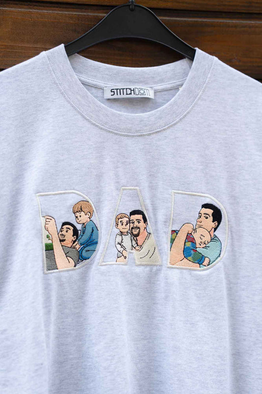 Tricou gri cu textul „DAD” brodat, fiecare literă conținând câte o imagine brodată reprezentând un tată și copilul.