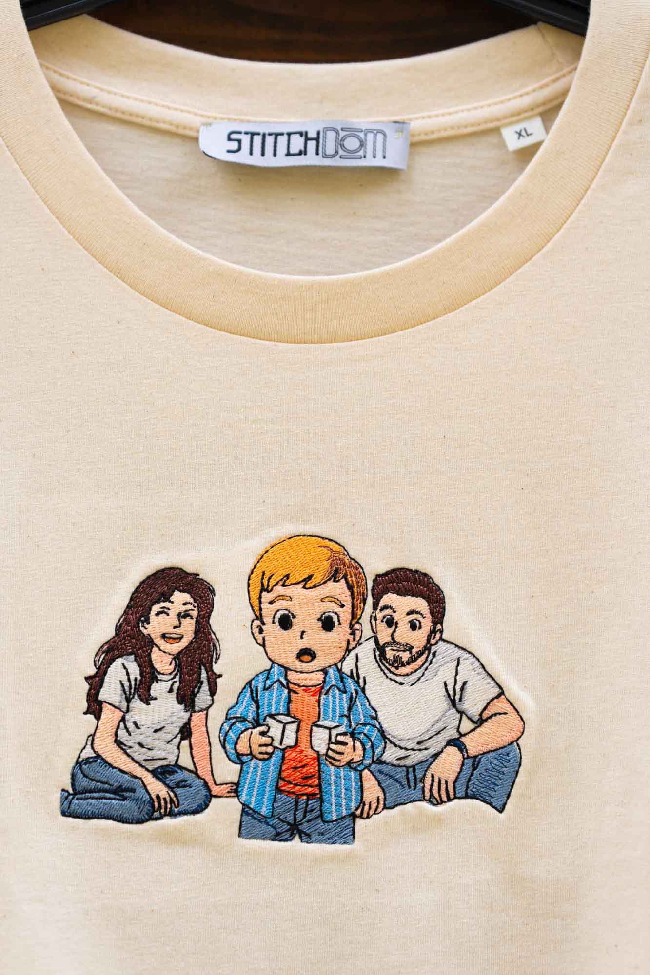 Tricou crem din bumbac organic, cu un model imprimat tip desen animat reprezentând trei personaje așezate împreună.