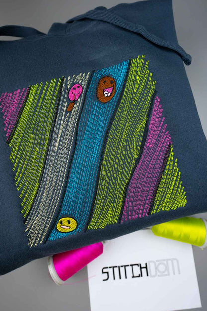 Hanorac bleumarin din bumbac organic, cu un model geometric colorat brodat, dupa poza unui copil, format din dungi verticale verde lime, verde petrol, gri și magenta, decorate cu mici fețe de personaje de desene animate, alături de conuri de ață și un card alb cu brandul „STITCHDOM” în prim-plan.