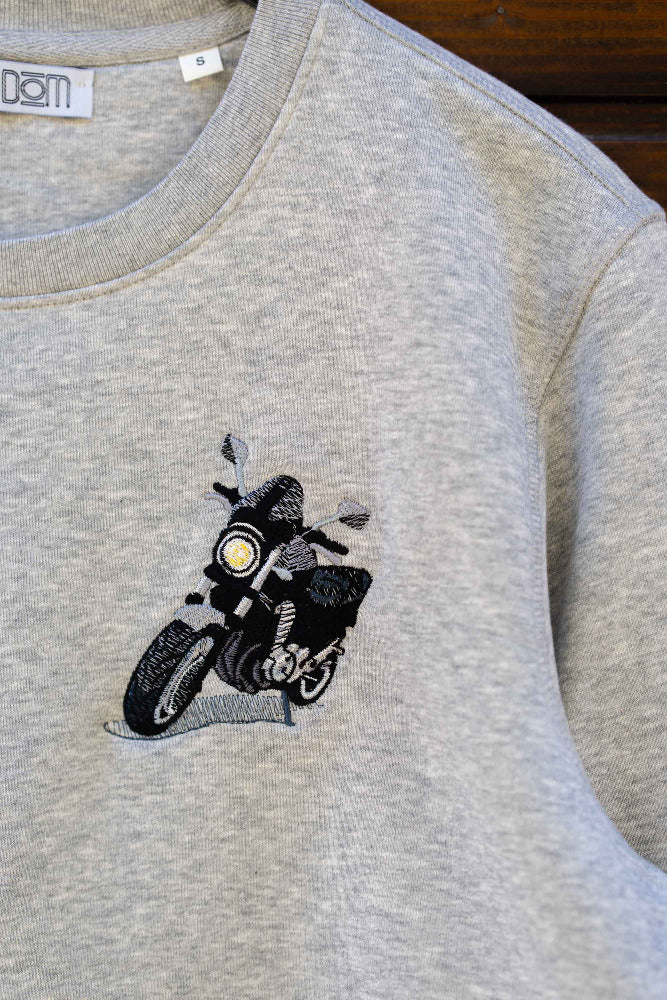 Bluza gri din bumbac organic, pe o suprafață din lemn, cu o poză brodată cu o motocicletă.