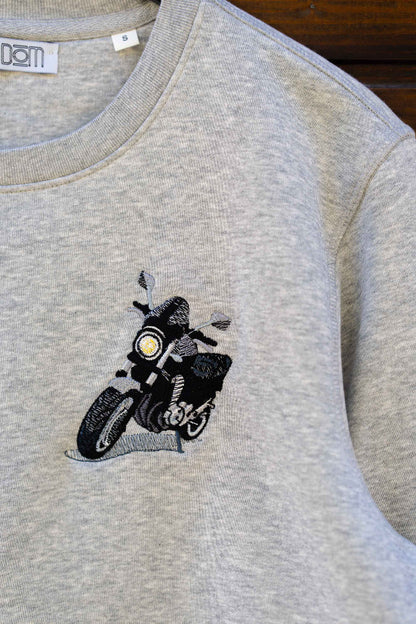 Bluza gri din bumbac organic, pe o suprafață din lemn, cu o poză brodată cu o motocicletă.