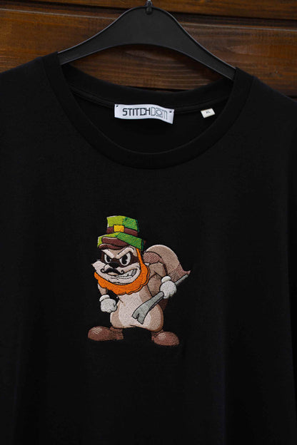 Tricou negru din bumbac organic, cu guler rotund, agățat pe un umeraș negru, pe un fundal din lemn închis, cu o poză brodată reprezentând personajul cartoon Louie the Lemur ținând un târnăcop, cu o etichetă „Stitchdom” vizibilă la gât.