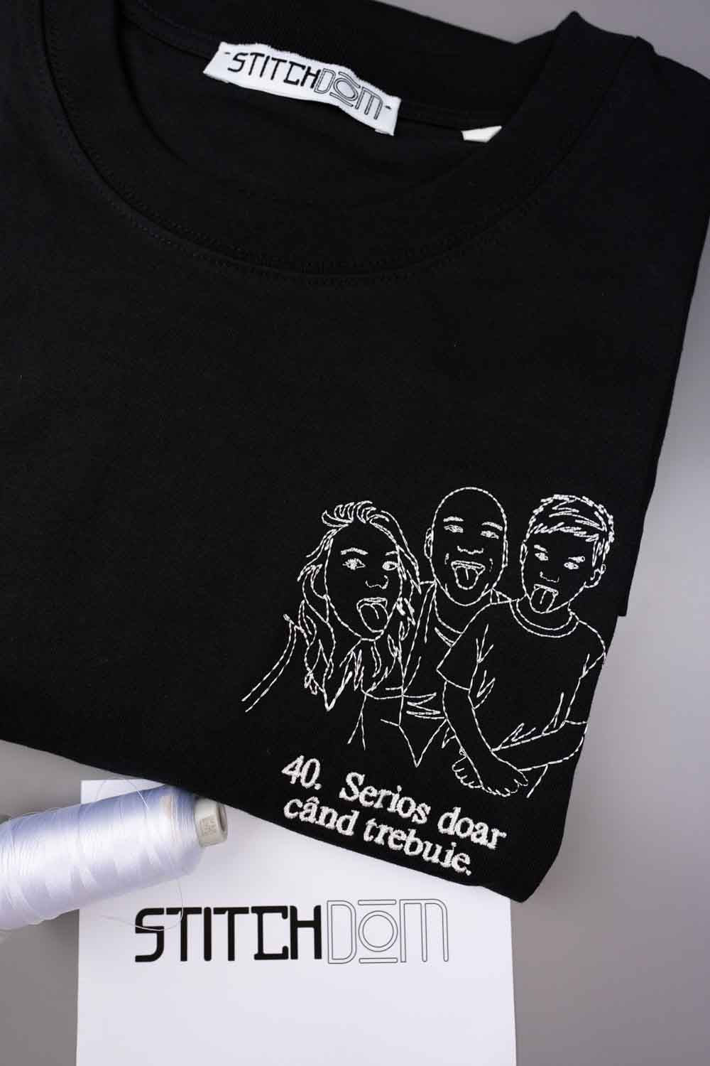 Tricou negru din bumbac organic, împăturit, cu o ilustrație albă brodată în stil line-art, reprezentând trei persoane care scot limba, alături de textul „40. Serious doar and trebie” brodat pe partea din față.