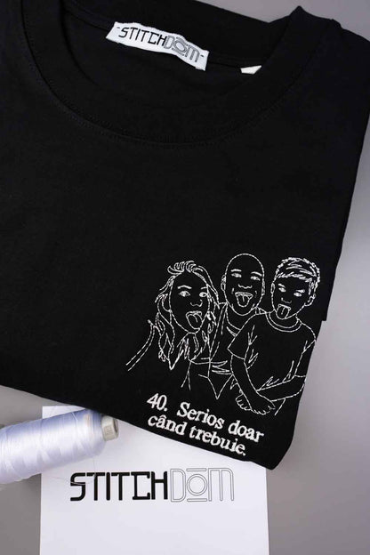 Tricou negru din bumbac organic, împăturit, cu o ilustrație albă brodată în stil line-art, reprezentând trei persoane care scot limba, alături de textul „40. Serious doar and trebie” brodat pe partea din față.