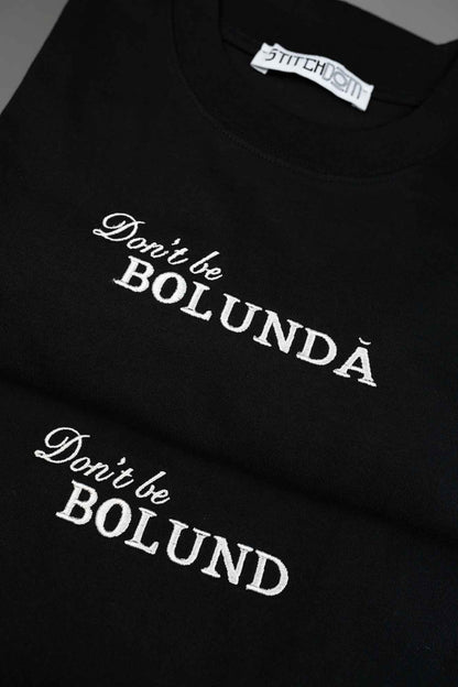 Tricou negru din bumbac organic, cu textele albe „Don't be BOLUNDĂ” și „Don't be BOLUND” brodate, cu o parte din eticheta interioară „Stitchdom” vizibilă.