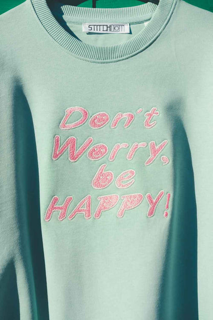 Hanorac verde mentă din bumbac organic, cu textul „Don't Worry, be HAPPY!” brodat cu roz pe piept și eticheta „STITCHDOM” vizibilă în interiorul gulerului.