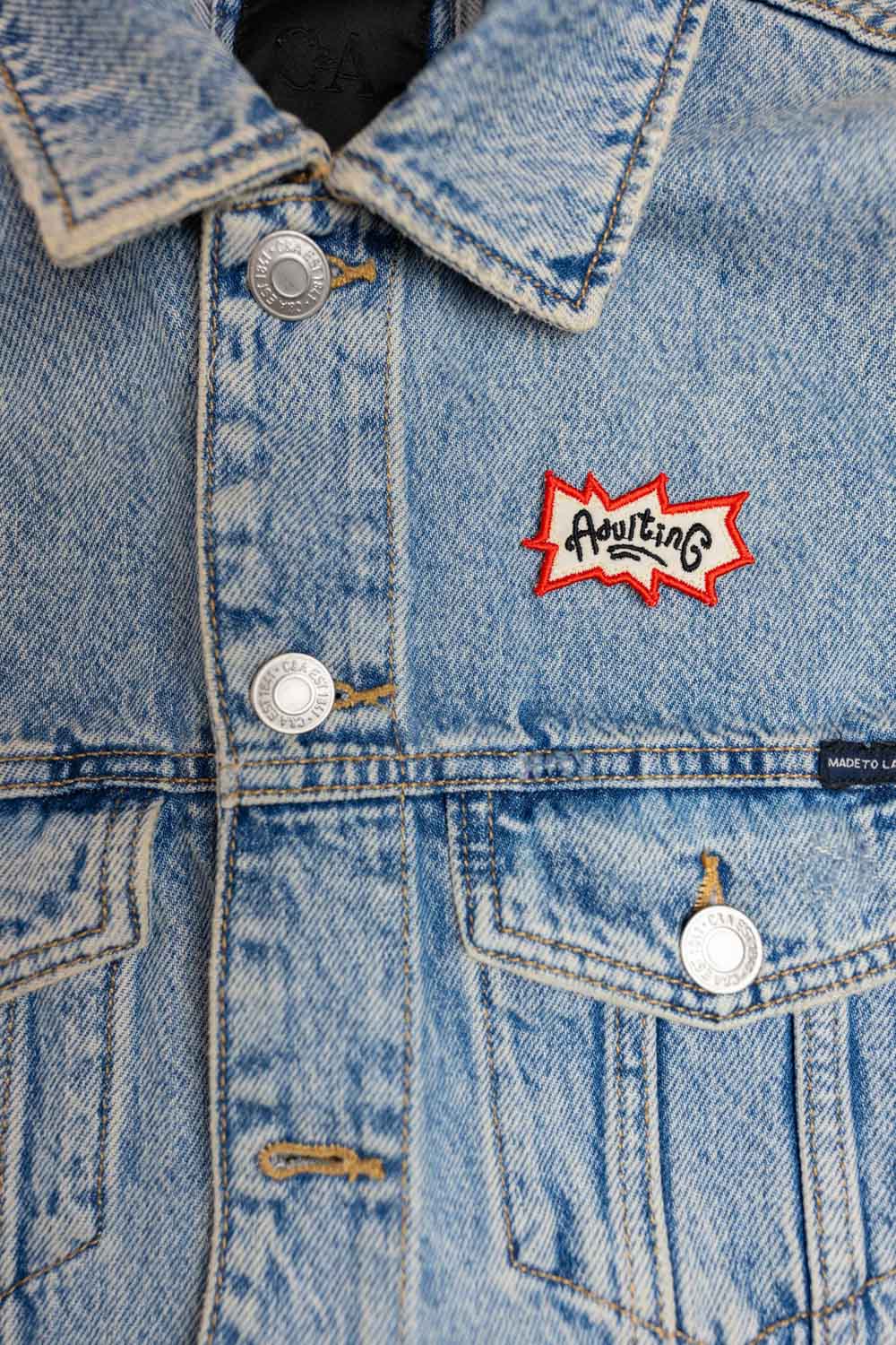 Patch brodat negru cu logo-ul „Adulting” în roșu și alb, un accesoriu ironic pentru viața de adult.