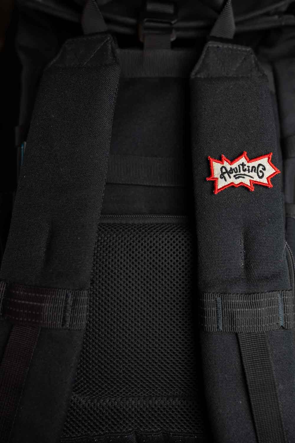 Patch brodat negru cu logo-ul „Adulting” în roșu și alb, un accesoriu ironic pentru viața de adult.