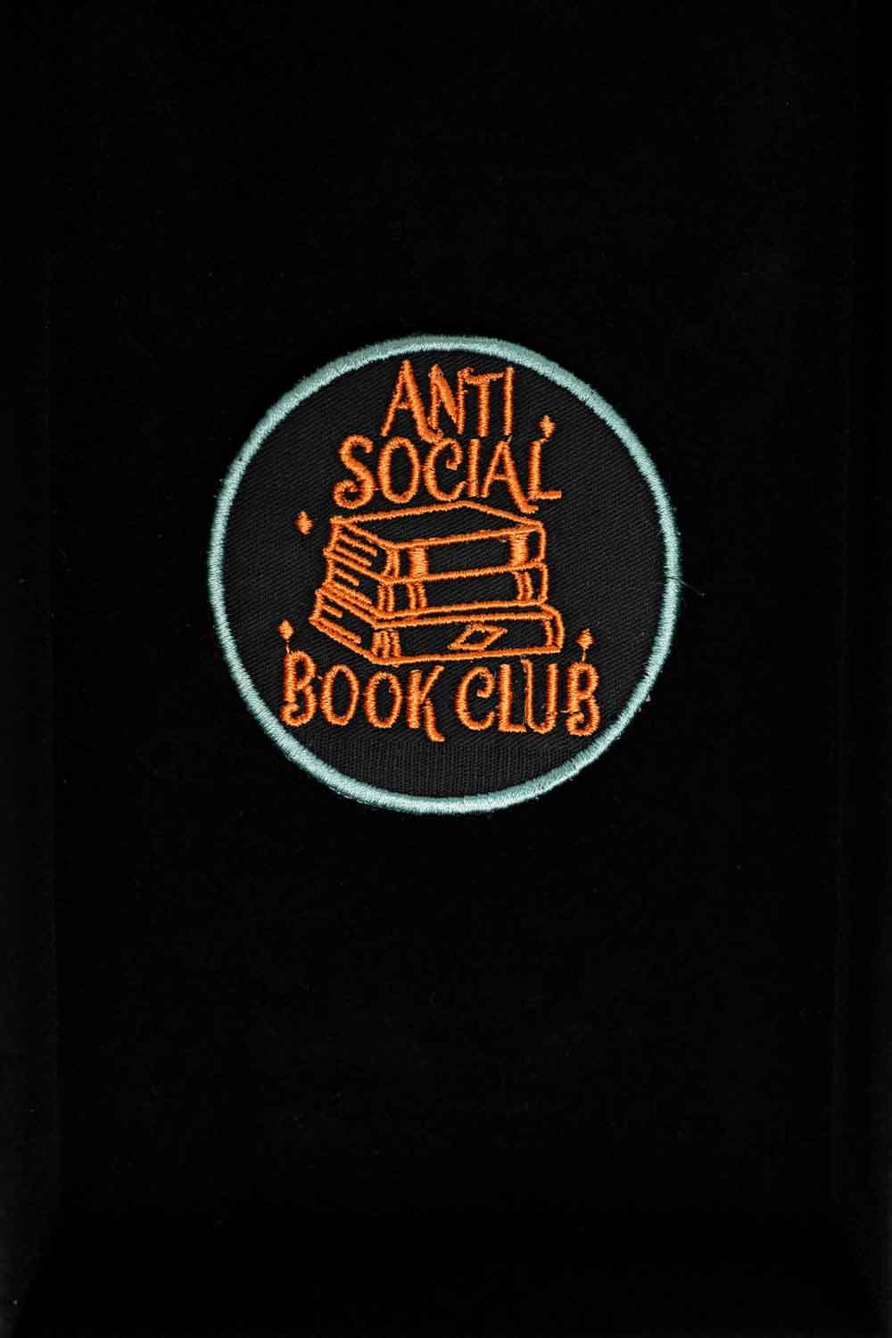 Patch brodat negru cu mesajul „Anti Social Book Club” și ilustrație de cărți, un accesoriu pentru pasionații de lectură.
