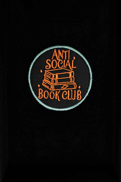 Patch brodat negru cu mesajul „Anti Social Book Club” și ilustrație de cărți, un accesoriu pentru pasionații de lectură.
