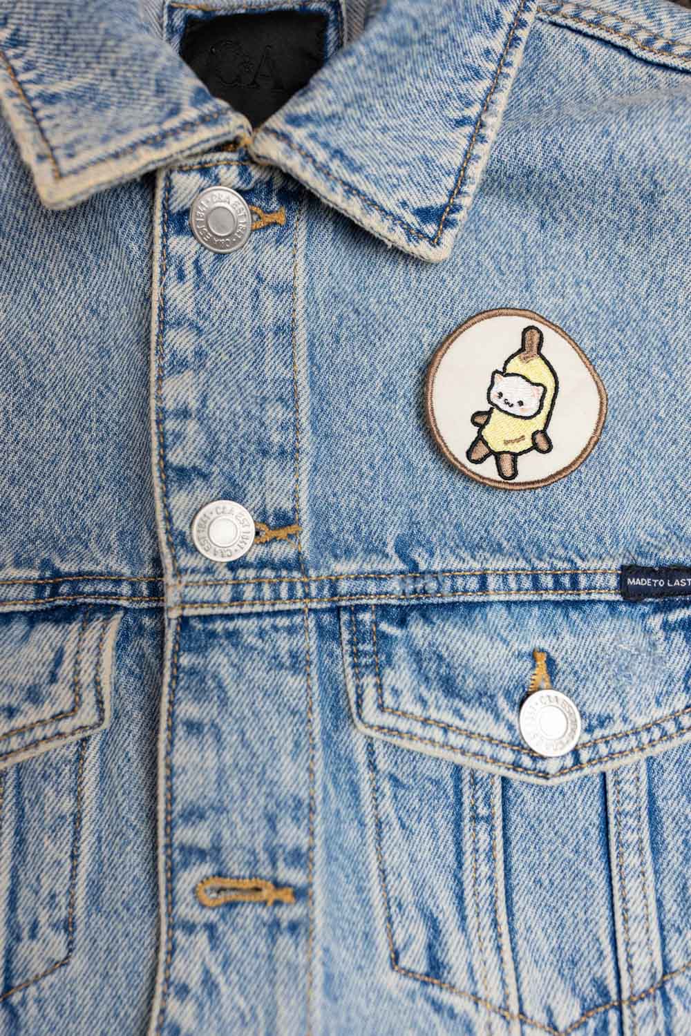 Patch brodat cu ilustrație de pisicuță într-o banană, un design kawaii și amuzant pentru personalizarea hainelor și genților.