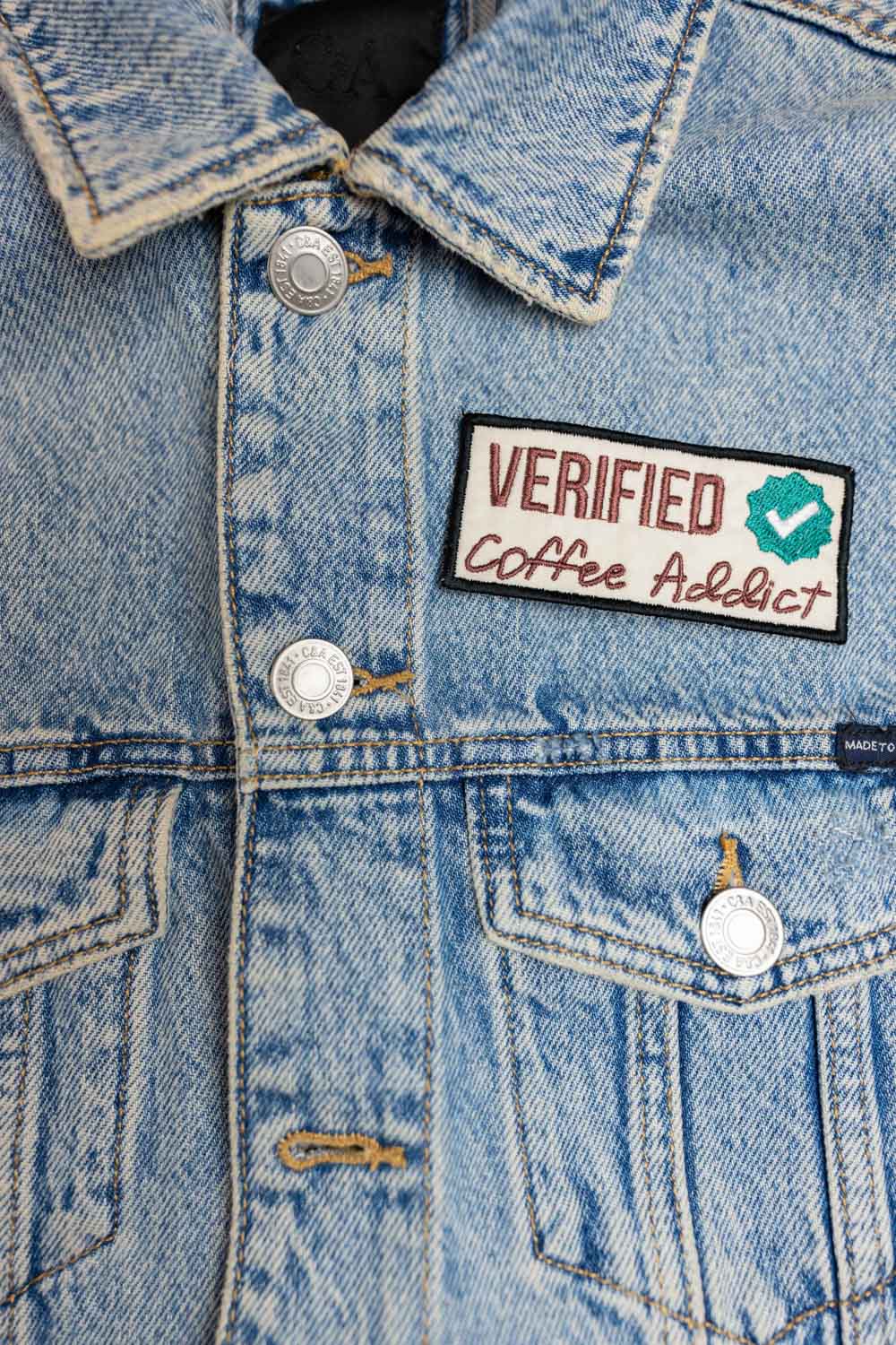 Patch brodat cu mesajul „Verified Coffee Addict” și simbol de verificare, un accesoriu perfect pentru iubitorii de cafea.