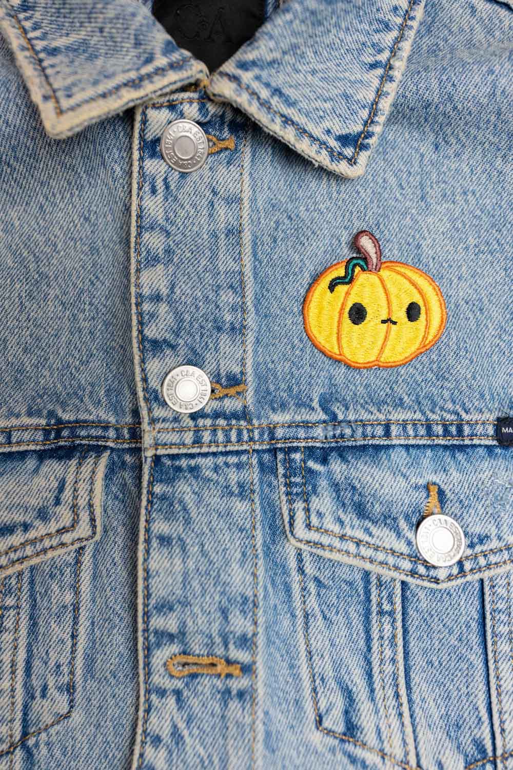 Patch brodat în formă de dovleac zâmbitor pe fundal negru, un accesoriu amuzant pentru Halloween, potrivit pentru personalizarea hainelor sau genților.