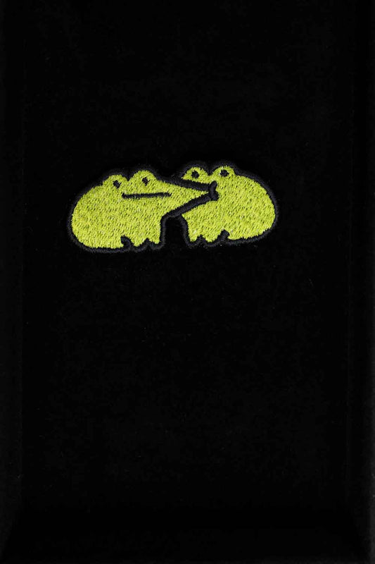 Patch brodat cu design de broască galbenă pe fundal negru, un accesoriu colorat și amuzant pentru haine, genți sau accesorii.