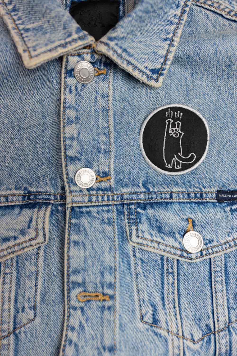 Patch brodat negru cu design alb al unei lăbuțe de pisică întinsă în sus, un accesoriu amuzant și creativ pentru personalizare.