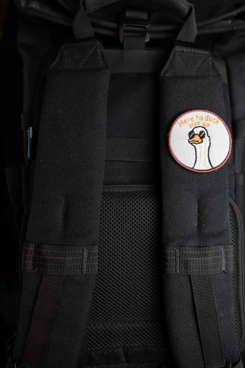 Patch brodat rotund cu ilustrație de cap de rață și mesajul amuzant „Here to Duck Shit Up”, un accesoriu ironic și creativ.