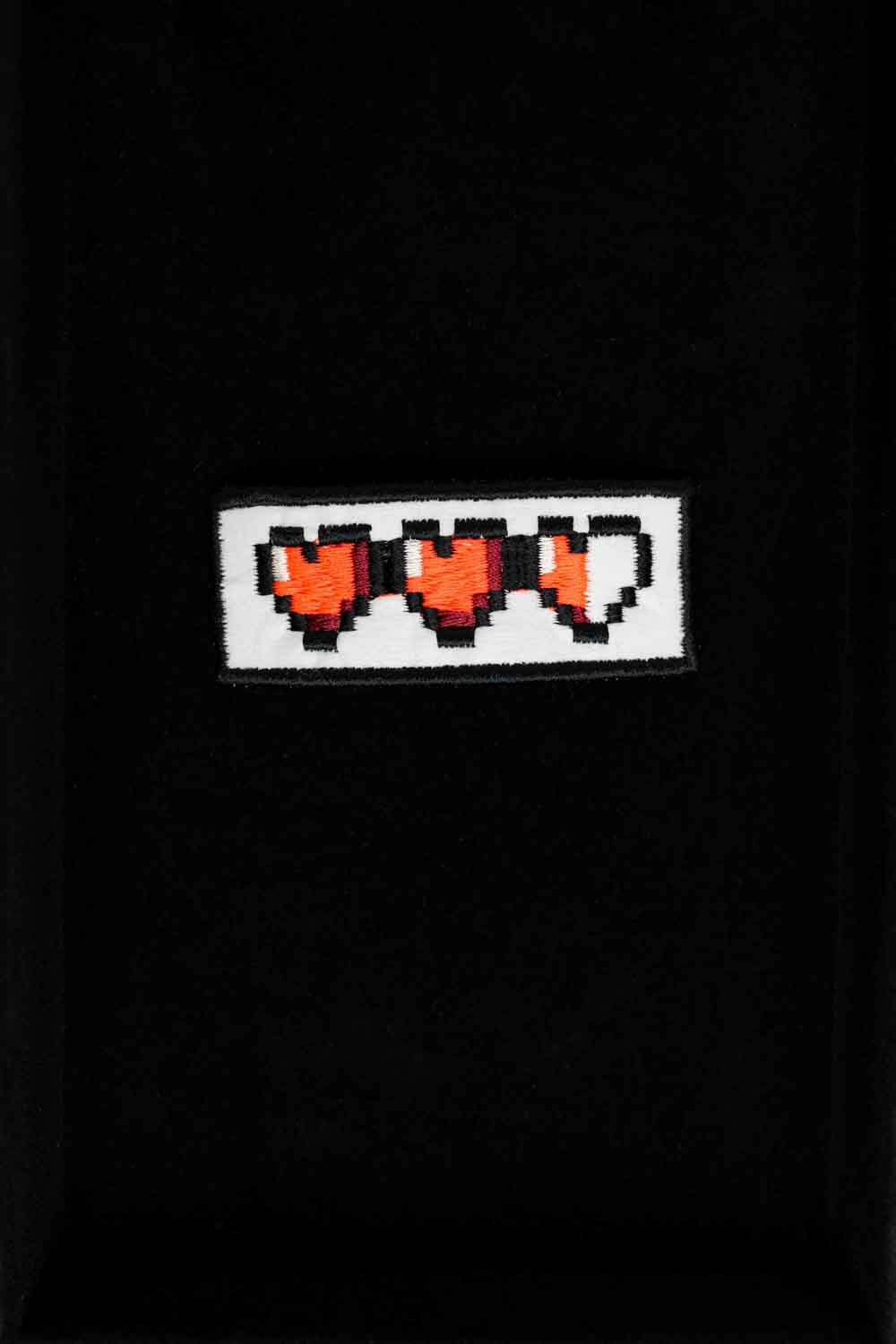 Patch brodat negru cu o serie de inimi pixel roșii, un accesoriu inspirat de stilul gaming retro.