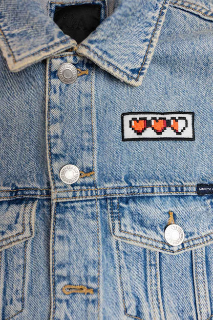 Patch brodat negru cu o serie de inimi pixel roșii, un accesoriu inspirat de stilul gaming retro.