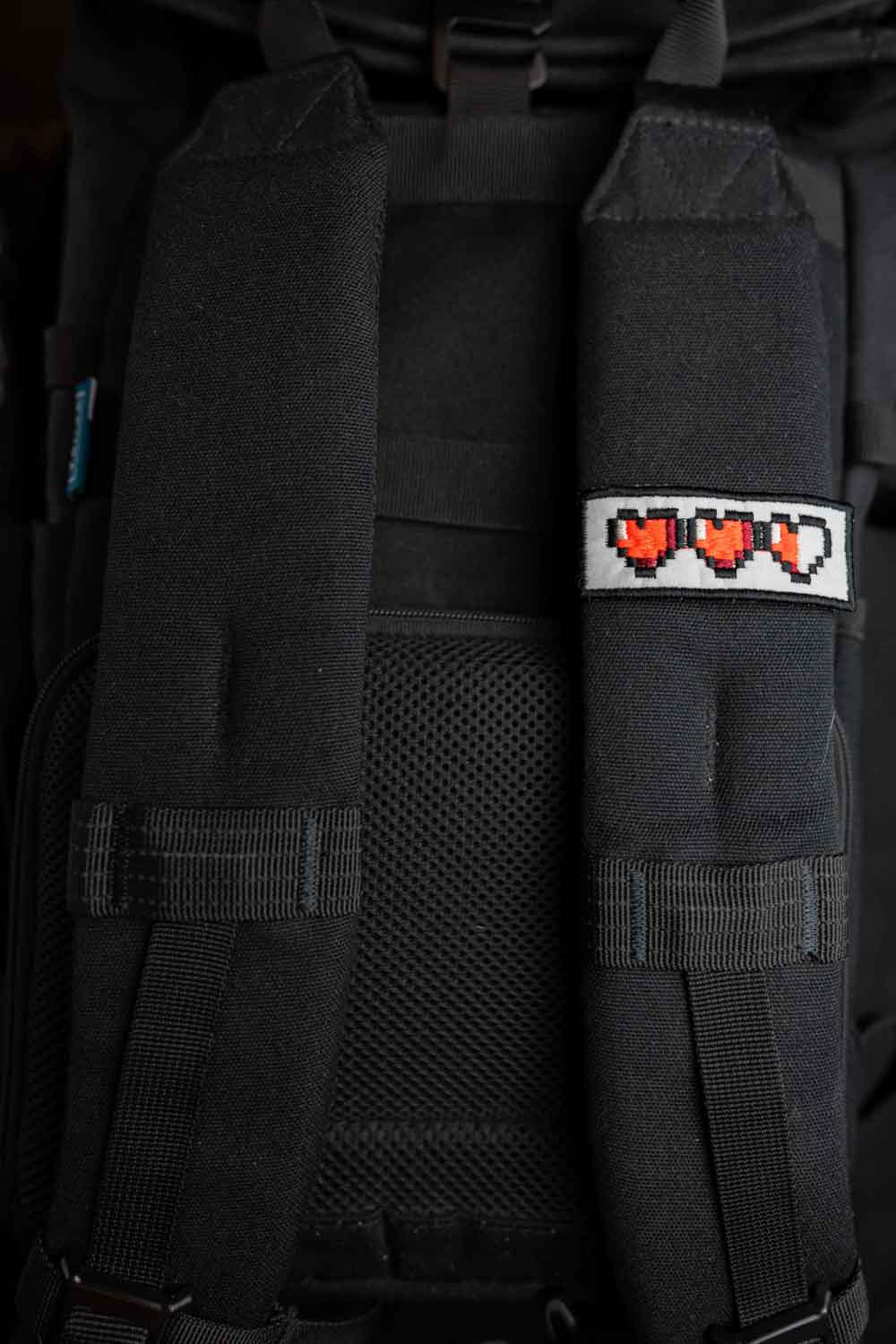 Patch brodat negru cu o serie de inimi pixel roșii, un accesoriu inspirat de stilul gaming retro.