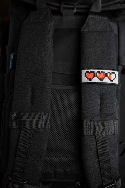 Patch brodat negru cu o serie de inimi pixel roșii, un accesoriu inspirat de stilul gaming retro.