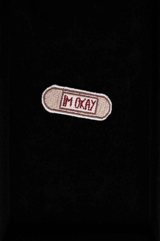 Patch brodat cu mesajul „I'm Okay” pe fundal bej, un accesoriu minimalist cu mesaj ironic și expresiv.