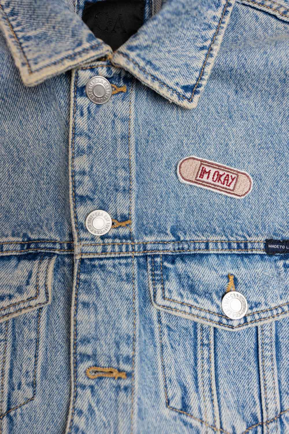 Patch brodat cu mesajul „I'm Okay” pe fundal bej, un accesoriu minimalist cu mesaj ironic și expresiv.