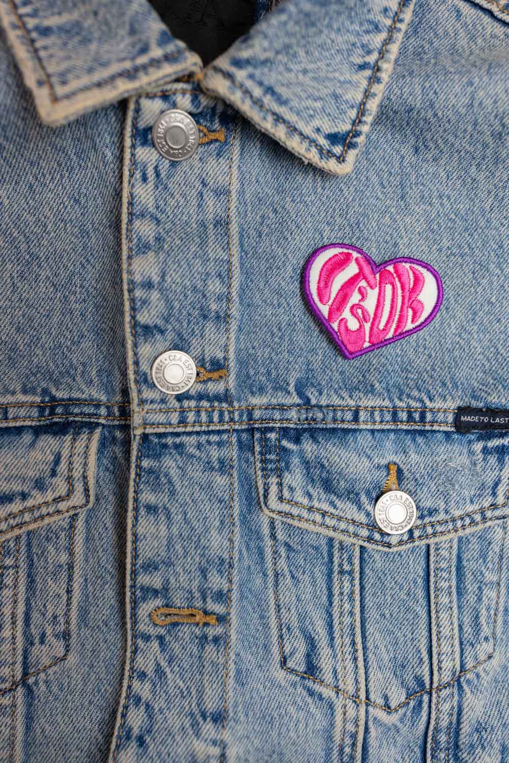 Patch brodat în formă de inimă roz cu mesajul „It's Ok”, un accesoriu delicat și expresiv.