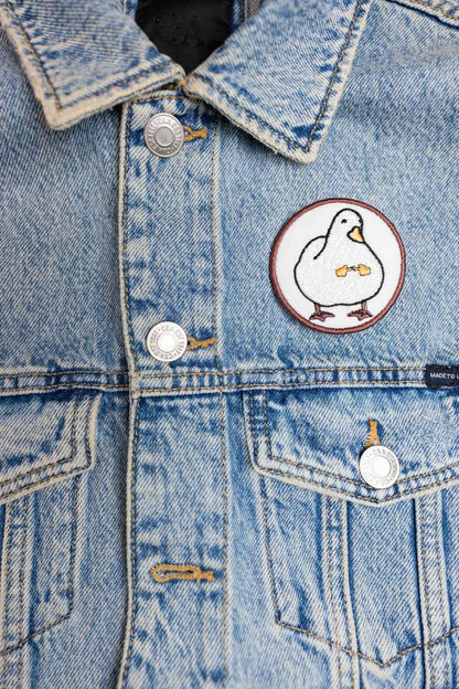 Patch brodat rotund cu fundal alb și roșu și o rață albă stilizată în centru, un accesoriu kawaii și colorat.