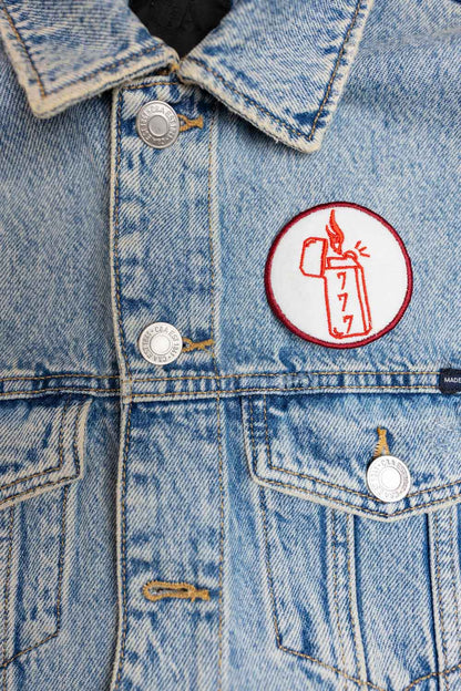 Patch brodat rotund cu design de brichetă, flacără și cifre în culori roșu și alb, un accesoriu original pentru haine și genți.