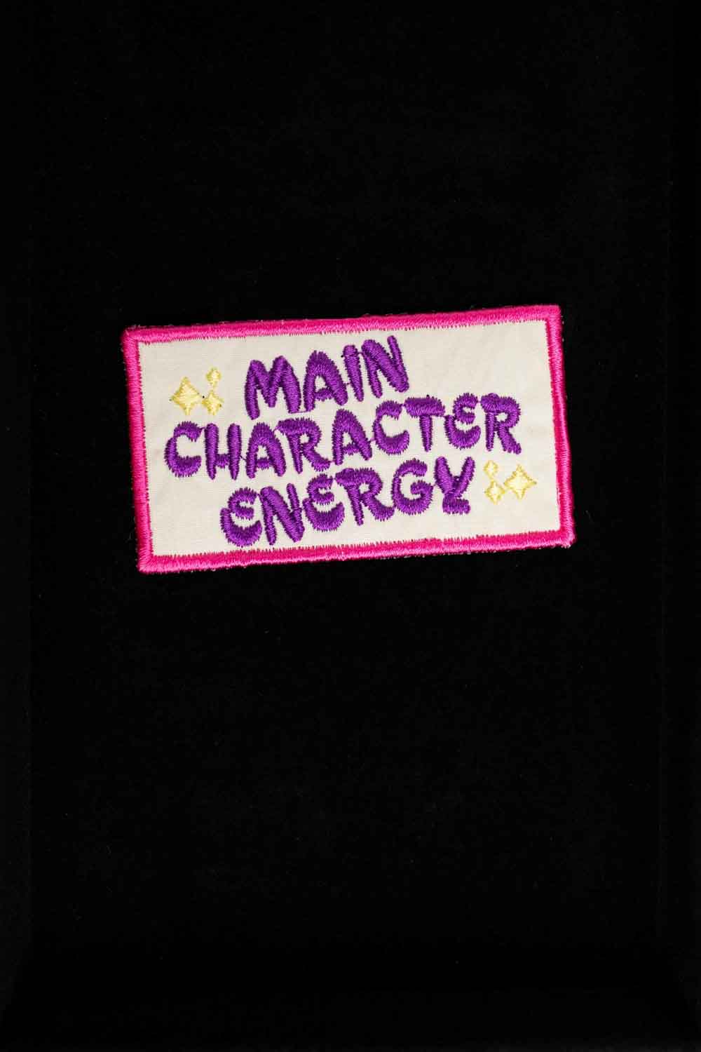 Patch brodat negru cu margine roz și mesajul „Main Character Energy”, un accesoriu amuzant și expresiv.