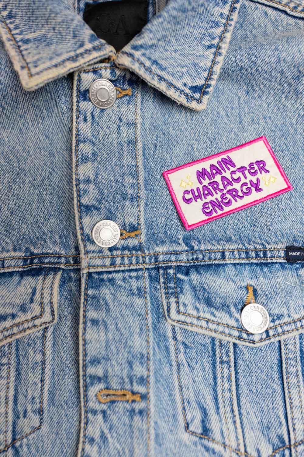 Patch brodat negru cu margine roz și mesajul „Main Character Energy”, un accesoriu amuzant și expresiv.