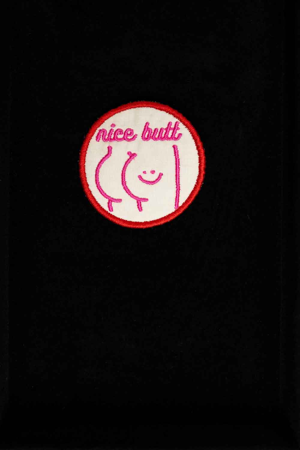 Patch brodat cu mesajul amuzant „Nice Butt” și față zâmbitoare, un accesoriu ironic și jucăuș pentru personalizare.